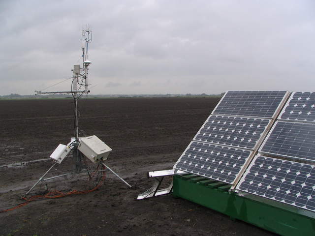 Solar panels and eddy tower at edge or rice field with overcast skies