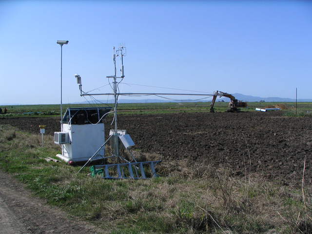Equipment box and eddy tower at edge of plowed rice field