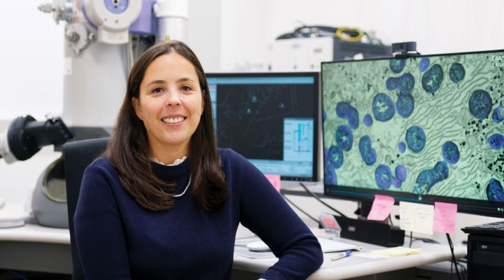 A woman smiling at the camera with a screen with molecules on it